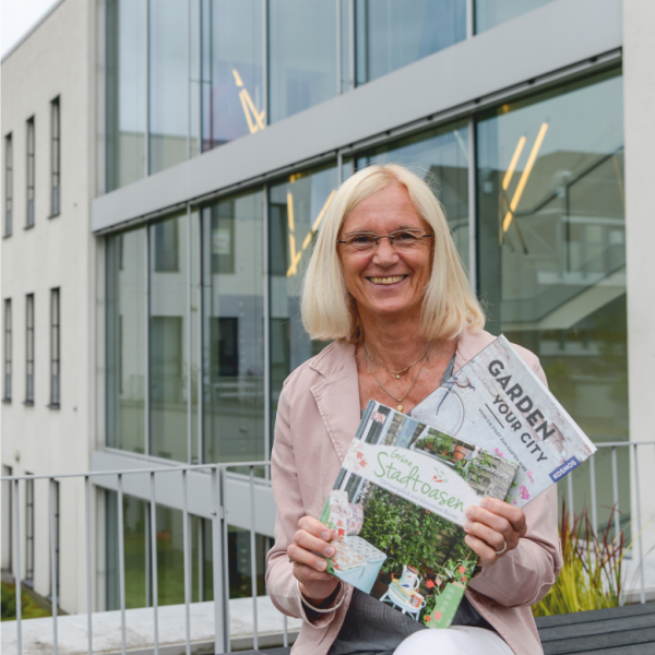 Frau vom Felde, Leiterin der Stadtbibliothek im Medienhaus, vor dem hinteren geäudeteil des Medienhauses mit zwei Büchern in der Hand