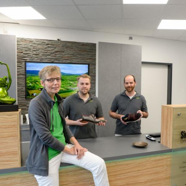 Auf dem Foto sieht man eine Frau und zwei Männer, die Schuhe in der Hand haben und ein Teil des Teams von Bausdorf Orthopädie bilden