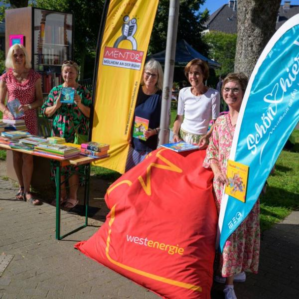 Fünf Frauen präsentieren an einem Büchertisch die gemeinsame Schön hier: Aktion, nämlich gebrauchte Kinderbücher kostenlos zu verteilen. Sie halten alle je ein Kinderbuch in der Hand. Auf dem Bild sind auch Fahnen zu sehen: Die Fahne der Lesementoren und eine Schön hier!-Fahne sowie ein roter Sitzsack von Westenergie | Foto: Walter Schernstein