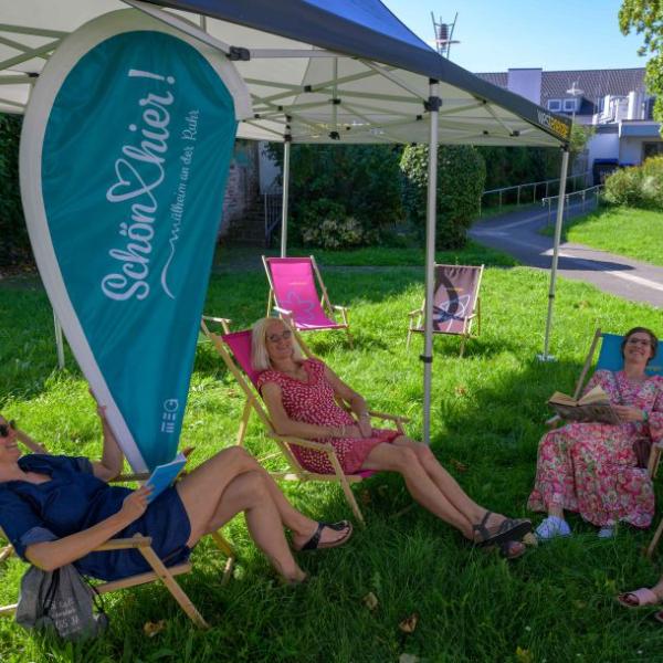 Drei Frauen liegen in einem kleinen Park unter einem Pavillon in Liegestühlen. Auch eine hellblaue schön hier!-Fahne ist zu sehen | Foto: Walter Schernstein