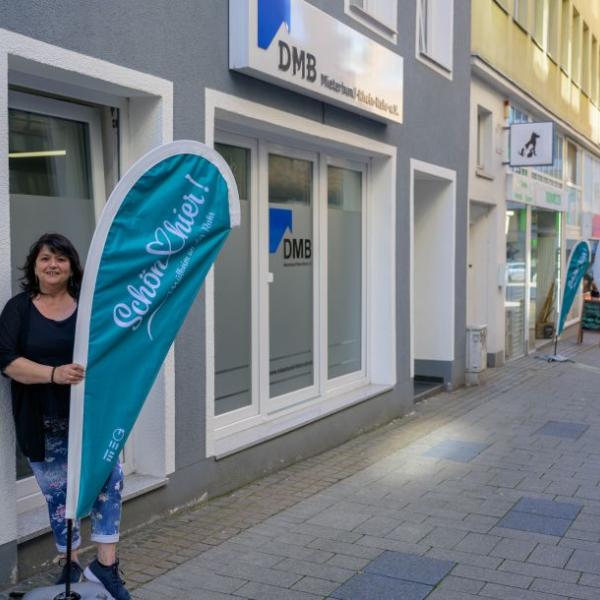 Eine Frau steht vor einem Ladengeschäft und hält die hellblaue Schön hier!-Fahne in der Hand | Foto: Walter Schernstein