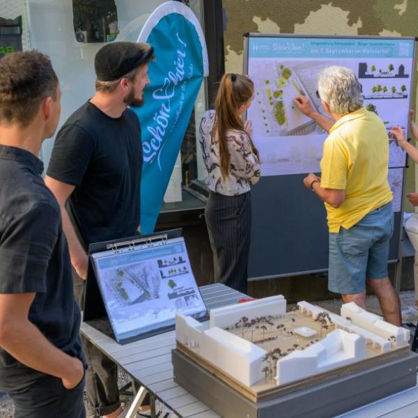 Einige Bürger*innen schauen sich die Planung des Rathausmarktplatzes auf einem Plakat an und lassen sich den Entwurf erläutern. | Foto: Walter Schernstein