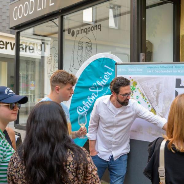 Einige Bürger*innen schauen sich die Planung des Rathausmarktplatzes auf einem Plakat an und lassen sich den Entwurf erläutern. | Foto: Walter Schernstein