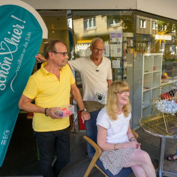 Zwei Männer stehen und eine Frau sitzt gut gelaunt vor einem Geschäft. Zu sehen ist auch die hellblaue Schön hier!-Fahne | Foto: Walter Schernstein