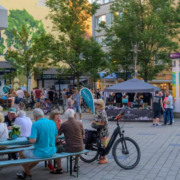 Passanten mit und ohne Fahrrad gehen durch einen mit hellblauer Schön hier!-Fahne geschmückten Straßenteil | Foto: Walter Schernstein